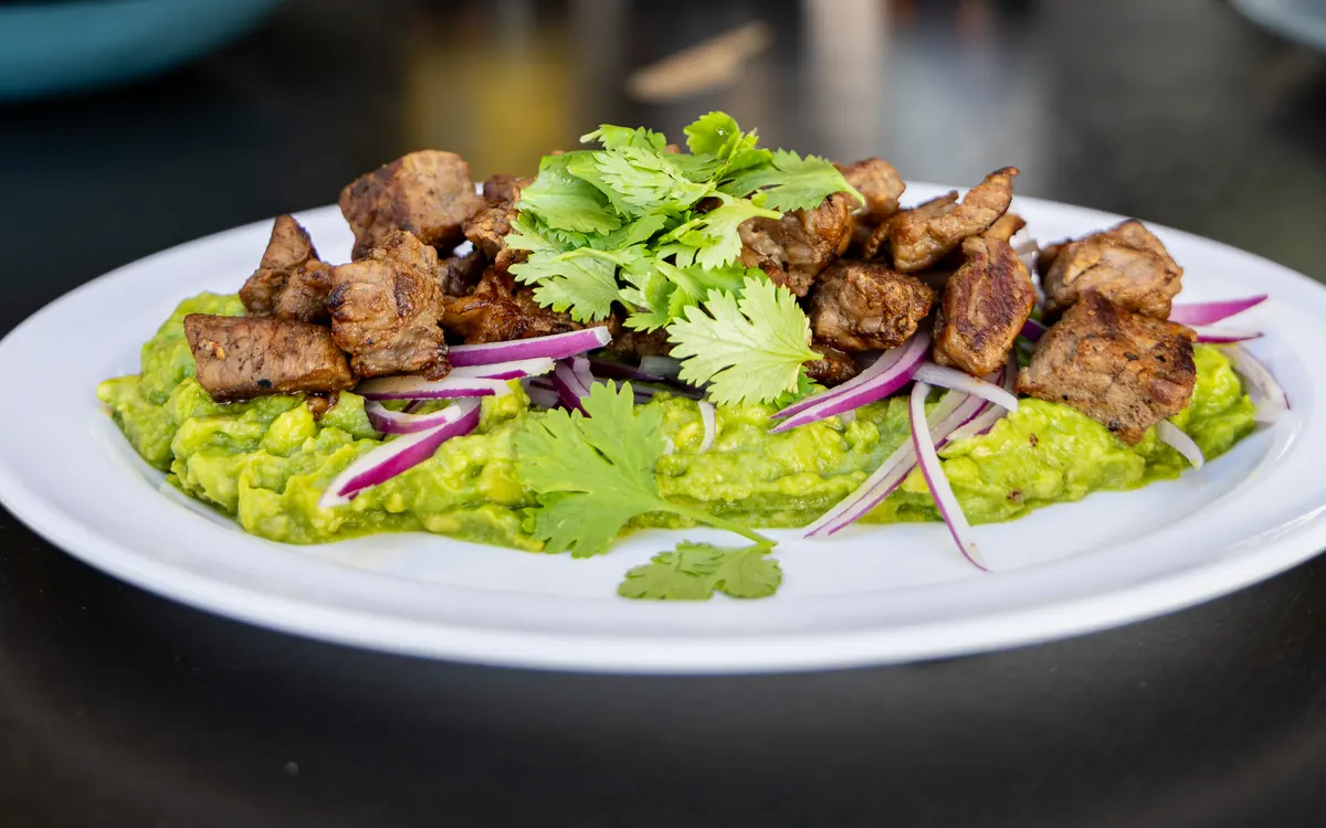 Ribeye sobre guacamole con cebolla morada en Patio Península